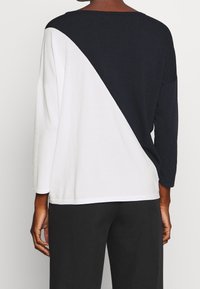 Top a maniche lunghe color block con sezioni nere e bianche, vestibilità morbida, scollo rotondo e texture del tessuto soffice. Presenta un dettaglio di cucitura curva.