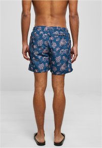 Bañador azul con estampado floral que presenta un patrón similar a corales, cinturilla elástica y bolsillos laterales. Fabricado con un tejido ligero y de secado rápido.