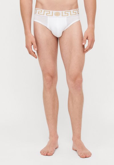 Bílé bavlněné slipy se zlatým vzorovaným pasem s designem řeckého klíče. Materiál vypadá hladce a přiléhavě, s minimálním pokrytím.