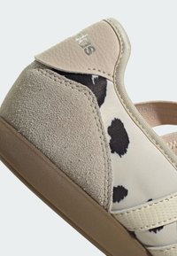 Talons de baskets beige avec panneaux en daim et cuir, tissu tacheté noir et blanc, et semelle en caoutchouc marron.