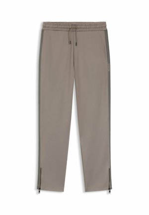 Taupe slim-fit track pants with elastic waistband, drawstring, side pockets, side stripe detailing, brand logo, and ankle zippers.