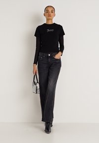 Čierne grafické tričko s nápisom „Juicy“, vrstvené na dlhom sieťovanom tričku s dlhým rukávom. Tmavé džínsy z denimu, úzky strih, doplnené striebornou kabelkou a čiernymi čižmami.