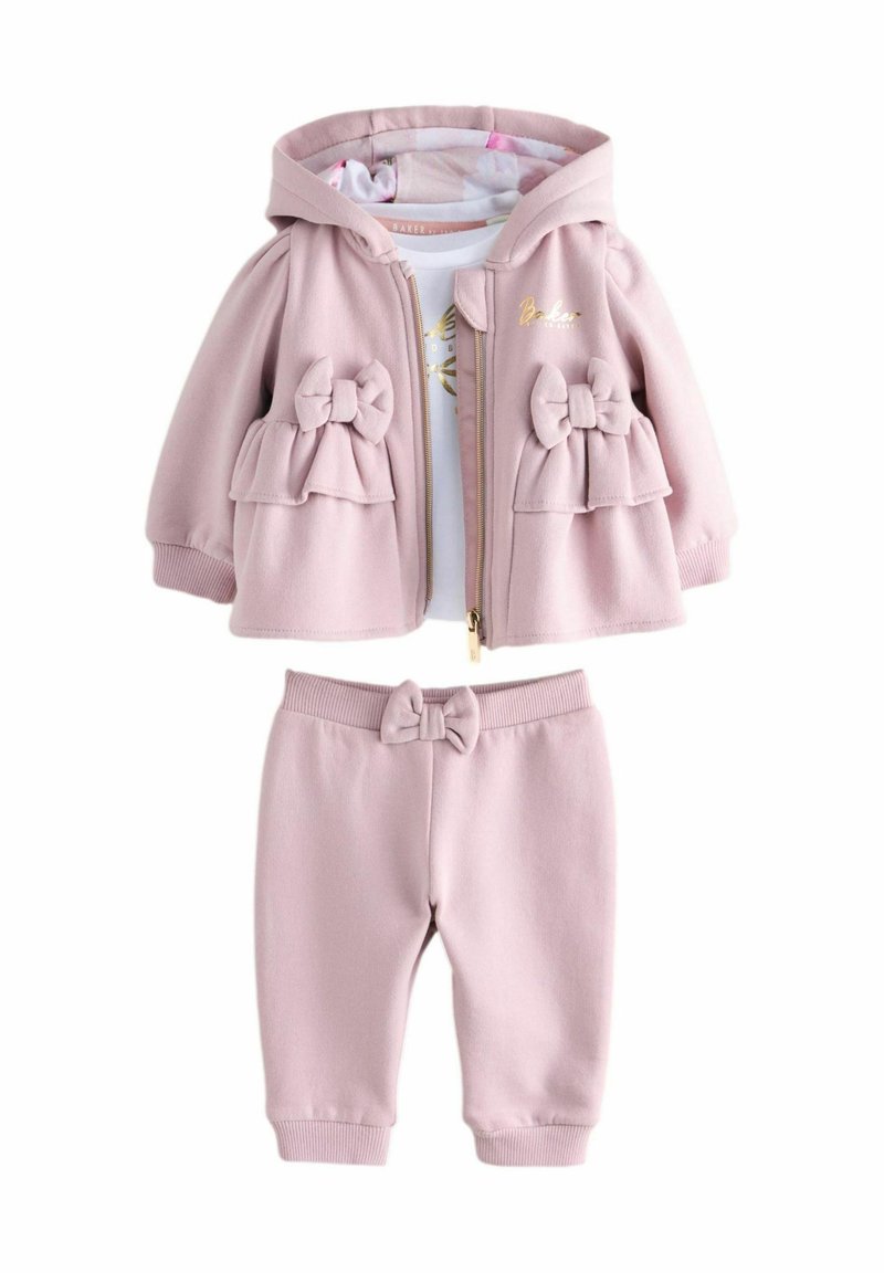 Béžová pink kapucňová bunda s detailmi mašle a zodpovedajúcimi elastickými nohavicami, doplnená o bielu košeľu s zlatým dizajnom.