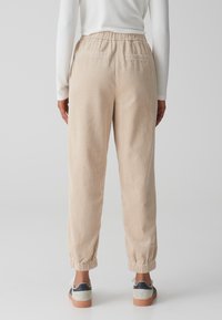 Beige corduroy broek met elastische tailleband, opgerolde enkels en twee achterzakken, gecombineerd met casual sneakers.