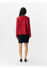 Röd stickad tröja med långa ärmar, kombinerad med en svart kjol. Outfiten har en avslappnad passform och en mjuk textur.