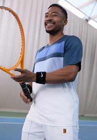Hvit tennis skjorte med marineblå og lyseblå striper, sammen med hvite shorts. Oransje racket holdt i hånden, svarte håndleddbånd, og en logo på skjorten.