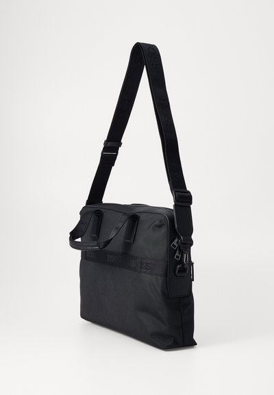 Sac messager noir en tissu texturé avec des poignées plates, une sangle réglable et un logo discret. Forme rectangulaire.