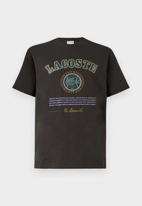 Černé bavlněné tričko s kulatým zeleným a žlutým potiskem, s výrazným nápisem "LACOSTE" a "TENNIS HERITAGE".