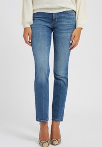 Jeans de denim azul claro con corte recto y un desgaste mínimo. Llevados con tacones estampados y un suéter crema.