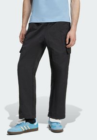 Czarne spodnie cargo o luźnym kroju, z kieszeniami bocznymi i lekką teksturą. W połączeniu z niebieskimi trampkami i jasnoniebieską koszulką.