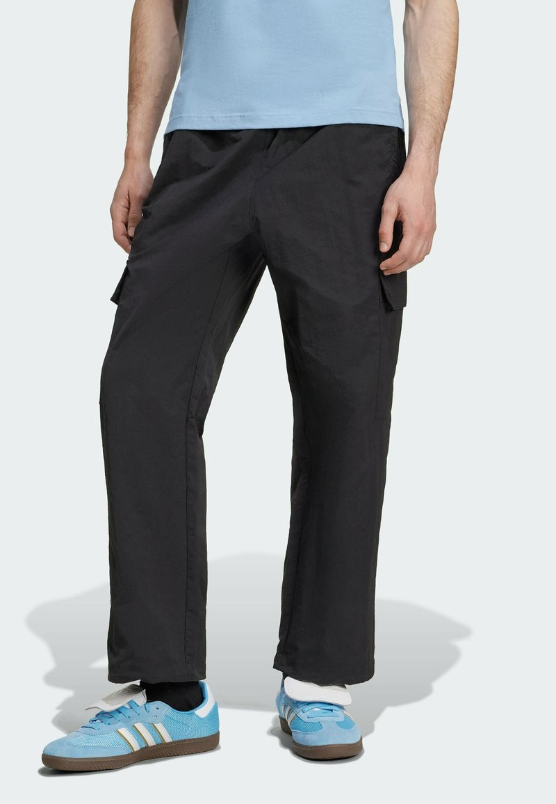 Czarne spodnie cargo o luźnym kroju, z kieszeniami bocznymi i lekką teksturą. W połączeniu z niebieskimi trampkami i jasnoniebieską koszulką.