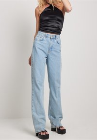 Jeans in denim blu chiaro a vita alta con gamba dritta, abbinati a un top halter in raso nero e sandali platform neri chunky.