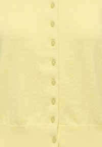 Gaiši dzeltena adīta kardigans ar mazām atbilstošām apaļām pogām priekšpusē un ribota apmale apakšā.