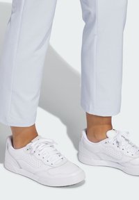 Λευκά αθλητικά παπούτσια με λείο δερμάτινο πάνω μέρος, στρογγυλή μύτη, διάτρητες λεπτομέρειες και επίπεδα κορδόνια, συνδυασμένα με ανοιχτό μπλε παντελόνια cropped.