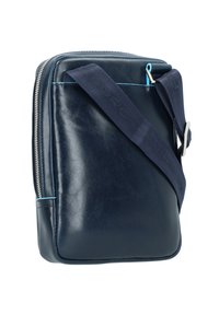 Marineblaue Ledertasche mit glatter Textur, Reißverschluss, verstellbarem Riemen und hellblauen Akzenten. Quadratische Form mit abgerundeten Ecken.