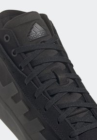 Černá sportovní obuv s texturovaným svrchním materiálem, plochými tkaničkami a gumovou podrážkou. Na jazyku je vyražené logo a výrazné panely.