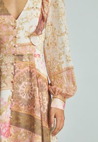 Sukienka w kwiatowy wzór, wykonana z miękkiego, lekkiego materiału; posiada głęboki dekolt w kształcie litery V, długie bufiaste rękawy oraz dekoracyjne guziki z przodu.