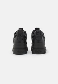 Black sneakers featuring a textured fabric upper, thick rubber sole, embossed branding, and padded collar for support.
