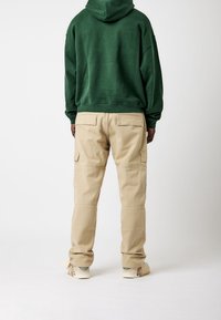 Sudadera verde con capucha y corte holgado, combinada con pantalones cargo beige que tienen grandes bolsillos y un diseño de pierna ligeramente entallado.