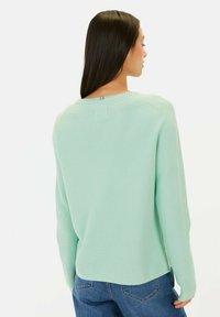 Mi�ętowa dzianinowa sweter z długimi rękawami, prążkowaną teksturą, okrągłym dekoltem i małym wycięciem na plecach, połączony z niebieskimi dżinsami.