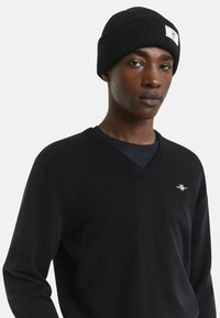 Berretto lavorato a maglia nero con risvolto e etichetta logo bianca, abbinato a un maglione nero a scollo a V con un piccolo logo sul petto.