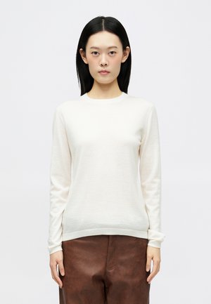 Suéter creme claro em tecido suave, com mangas longas, decote redondo e bainha justa, combinado com calças castanhas texturizadas.