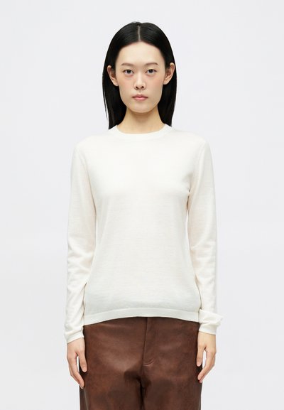 Maglione chiaro in morbido tessuto, con maniche lunghe, scollatura a girocollo e orlo aderente, abbinato a pantaloni marroni con texture.