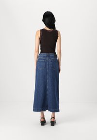 Black tank top with lace trim, paired with a long blue denim skirt featuring side slits and back pockets, worn with black heeled sandals.