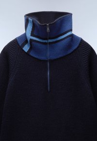 Granatowy sweter z dzianiny z wysokim kołnierzem, zdobiony niebieskim wzorem w paski oraz zamkiem błyskawicznym na ćwierć długości przy szyi.