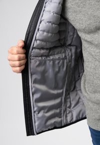 Schwarze Daunenjacke, Innenansicht zeigt gestepptes graues Futter und Innentasche, mit einer Hand offen gehalten. Strukturierter Außenstoff sichtbar.