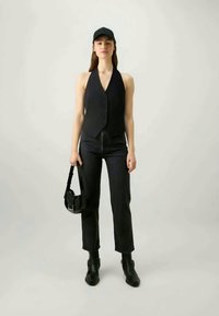Black sleeveless bodysuit with a v-neck and front buttons, paired with straight-leg black jeans and a small black shoulder bag.