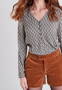 Košile s knoflíky v černobílé květinové vzoru; v kombinaci s hnědými vysokými manšestrovými šortkami. Texturovaná tkanina, uvolněný střih.