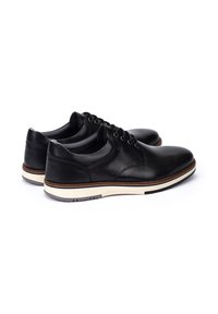 Zapatos de cuero negro con punta redondeada, que presentan un diseño de cordones, suela blanca y acentos marrones en la suela intermedia. Textura suave en general.