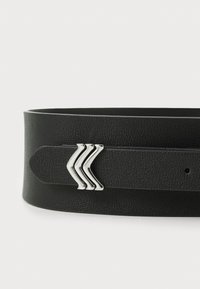 Cinturón de cuero negro con superficie texturizada, que presenta un acento de metal plateado suave con tres líneas curvas. Ajustable con agujeros para el cierre.