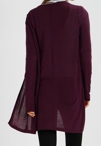 Tygkofta, djup burgunder, långa ärmar, asymmetrisk fåll, lätt material, med horisontella randmönster längs ryggen.