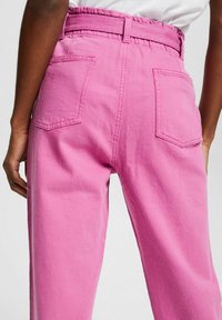Pantaloni in denim rosa con una vestibilità rilassata, dotati di tasche anteriori e posteriori, una vita alta con cintura e dettagli di cucitura a vista.