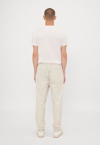 Ljust beige bomullbyxor med elastisk midja, sidofickor och muddar; bärs med en vit t-shirt med kort ärm och vita sneakers.