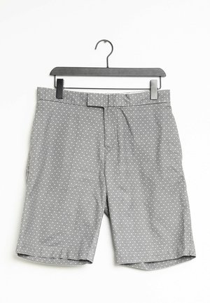Grå mønstrede shorts hængende på en sort plastik bøjle mod hvid baggrund.