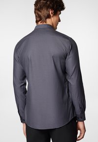 Ciemnoszara koszula z długim rękawem, z delikatnym wzorem strukturalnym, tradycyjnym kołnierzykiem i pojedynczymi czarnymi guzikami na mankietach.