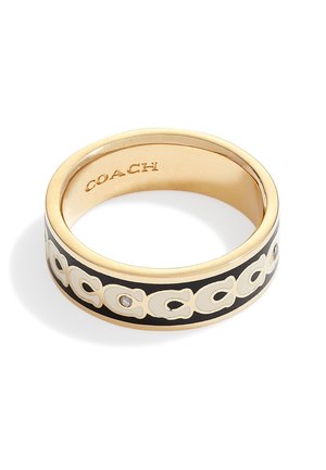 Pierścionek Coach w złotym odcieniu z czarną opaską, z powtarzającym się białym wzorem logo "C" i małym osadzonym kryształem, wewnątrz wygrawerowane "COACH".