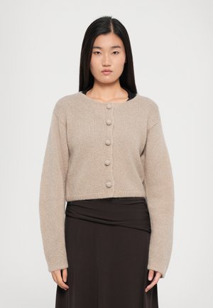 Lys beige kort cardigan laget av mykt strikket stoff, med seks runde knapper foran og lange, litt oversized ermer.