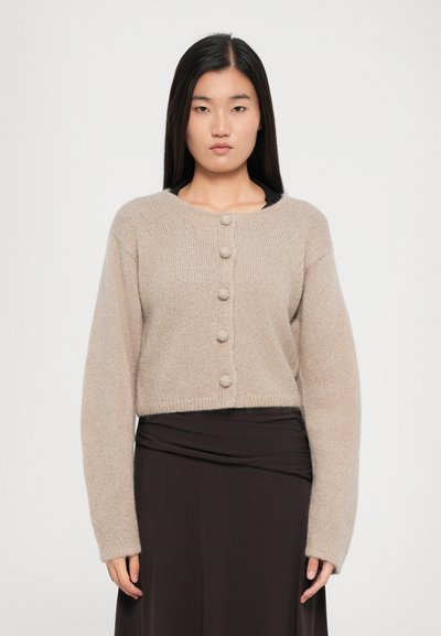 Lyse beige cropped cardigan lavet af blødt strikstof, med seks runde knapper fortil og lange, let oversize ærmer.