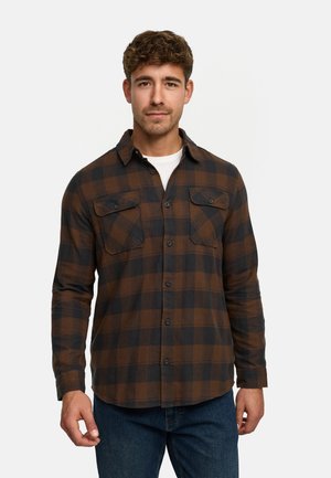 Camisa de franela a cuadros marrón y negro con cierre de botones en la parte delantera, dos bolsillos en el pecho y mangas largas, combinada con vaqueros azules.