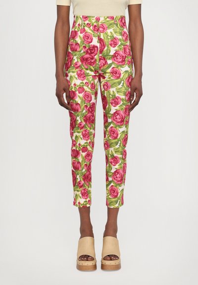 Pantalons fleuris arborant de grandes roses roses et des feuilles vertes sur un fond blanc, avec une taille haute et une coupe fuselée.