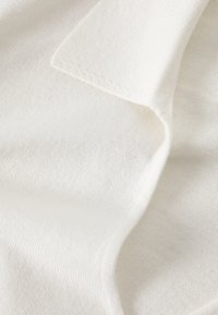 Țesătură albă tricotată cu o textură moale, având un model uniform și o dantelă ușoară pe marginile sale.