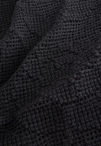 Tissu tricoté noir avec une texture gaufrée et un motif à tissage ouvert, plié pour montrer la profondeur et la douceur.