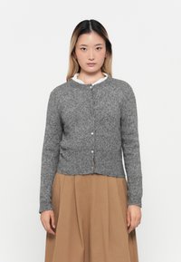 Grijze gebreide cardigan met ronde hals, knoopsluiting, ribbelrand en zachte textuur, gedragen over een wit shirt en een bruine rok.