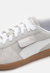 Baskets en cuir et daim gris avec des accents blancs, dotées de lacets blancs et d'une semelle en gomme texturée. L'étiquette du logo affiche "Puma Palermo".