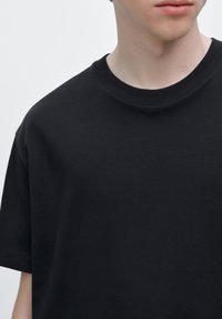 Svart oversize t-shirt med rund halsringning och korta ärmar, tillverkad av mjukt, slätt tyg; har minimalistiska sömdetaljer.