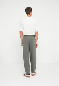 Sweatpants aus olivgrünem Stoff, mit lockerer Passform und elastischem Bund. Weißes T-Shirt sichtbar, mit schlichter Gestaltung und kurzen Ärmeln.